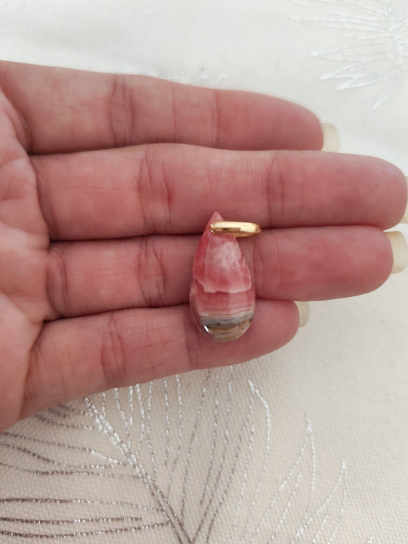 Pendentif rhodochrosite brute tenu en main - fond tissu blanc