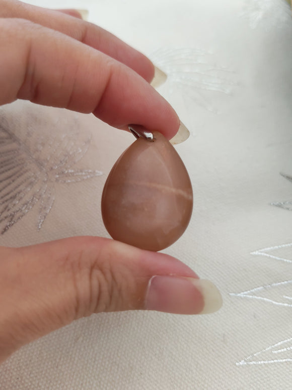 Pendentif larme pierre de soleil tenu en main - teintes caramel rosé